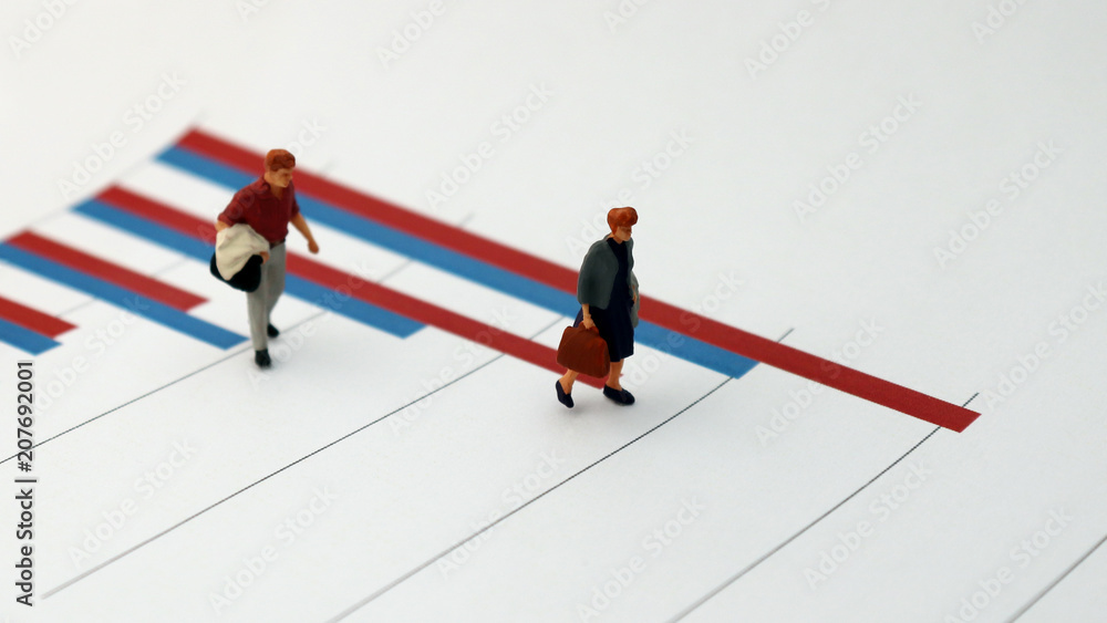 The concept of the widening income gap between people. Two miniature people standing on a bar graph. The concept of the widening income gap between people. Two miniature people standing on a bar graph.