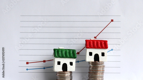 Housing price rising and differentiated concept. A miniature house on a pile of coins in front of a graph. photo
