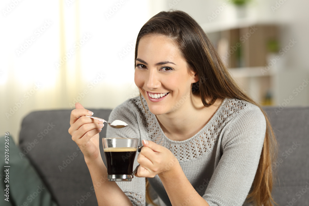 Happy woman throwing sugar into coffee looking at you Happy woman throwing sugar into coffee looking at you