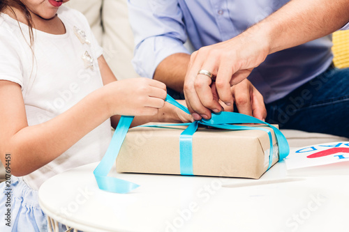 Little daughter giving her father a blue ribbon gift box for surprise at father's day.Love of family and father day concept