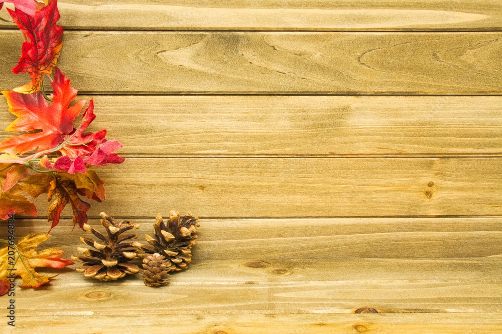 Three small pine cones and autumn leaves with a wood background providing copy space Three small pine cones and autumn leaves with a wood background providing copy space