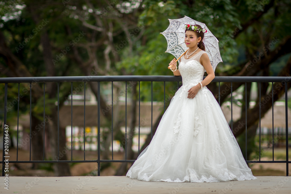 Young girl in a bridal gown holding a white umbrella on a steel bridge.