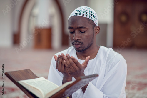 Black African Muslim Man Is Praying In The Mosque with open holy book of Koran