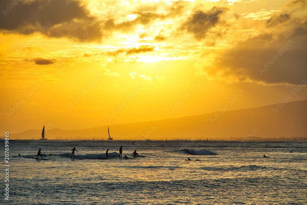 A group of surfers catching some waves off the coast of Oahu during sunset.