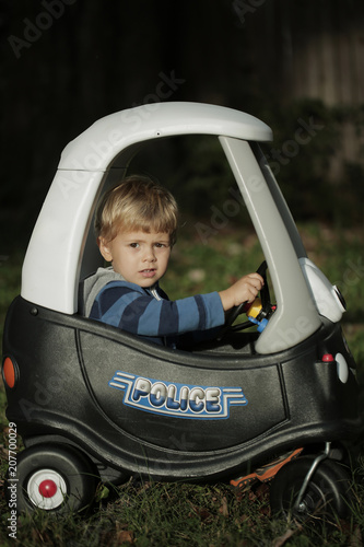 Blonde Little boy driving big toy police car outdoors