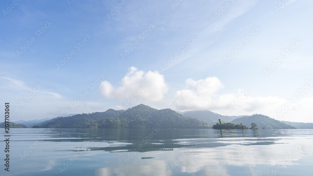 Beautiful high mountains and clear water at Cheow Lan Lake in Khao Sok National Park with morning light, reflection of blue sky and clouds on the sea.