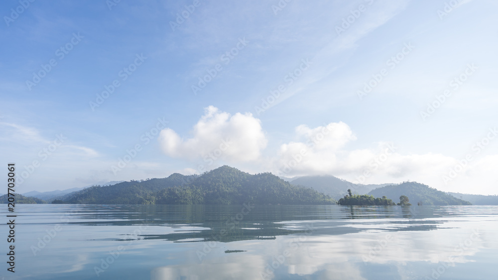 Beautiful high mountains and clear water at Cheow Lan Lake in Khao Sok National Park with morning light, reflection of blue sky and clouds on the sea. Beautiful high mountains and clear water at Cheow Lan Lake in Khao Sok National Park with morning light, reflection of blue sky and clouds on the sea.
