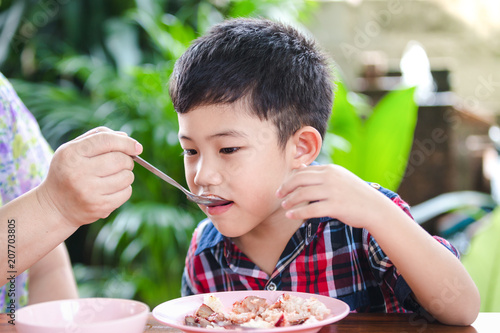 Asian little boy eating with rice food on the wooden table Mother feeding rice food