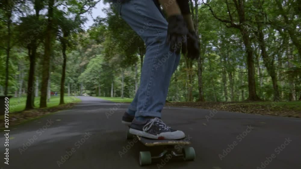 Front view follow shot of young man in helmet skateboarding in green park on summer day and looking ahead carefully Front view follow shot of young man in helmet skateboarding in green park on summer day and looking ahead carefully