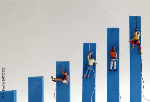 Miniature people climbing on hand blue bar graphs. The concept of competition for success. photo