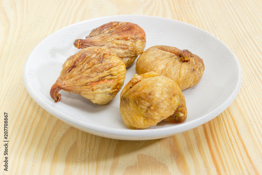 Dried figs on the white saucer on a wooden surface Dried figs on the white saucer on a wooden surface