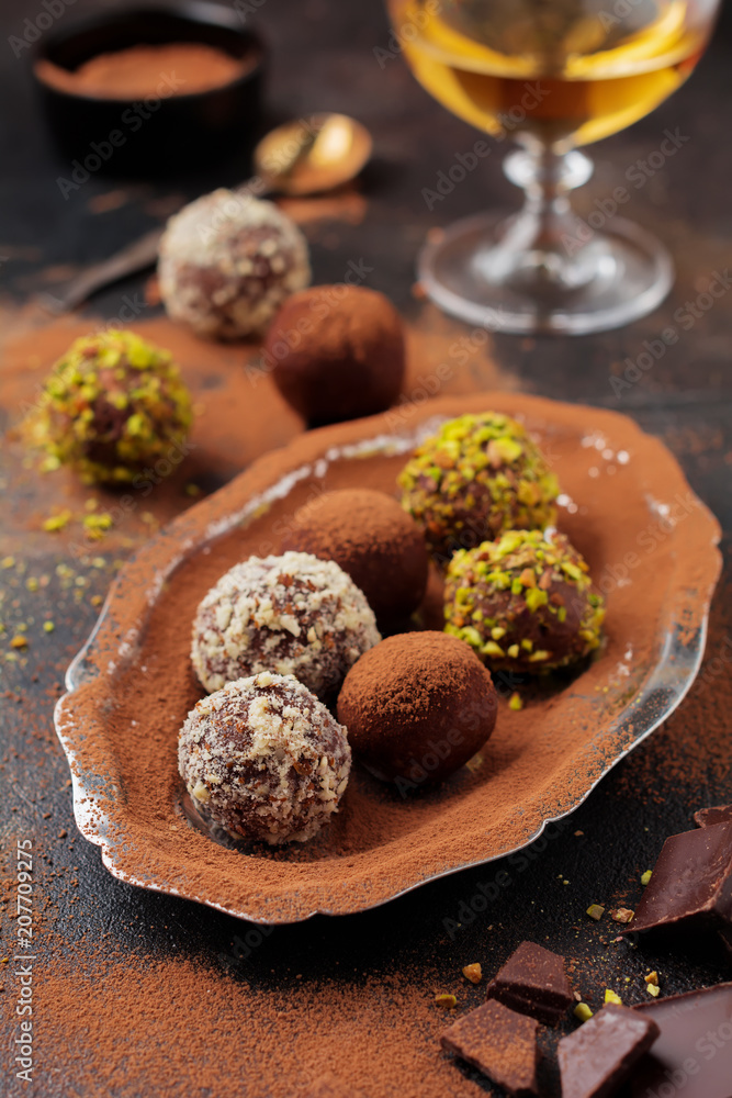 Variety of homemade dark chocolate truffles with cocoa powder, pistachios, almonds in dark brown background texture. Top view, copy space. Variety of homemade dark chocolate truffles with cocoa powder, pistachios, almonds in dark brown background texture. Top view, copy space.