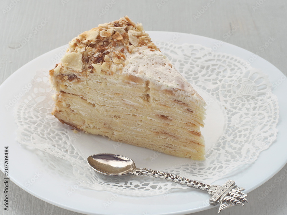 Slice of mille feuille on white plate with funny spoon in a shape of ship. Multi layered cake. Selective focus. Slice of mille feuille on white plate with funny spoon in a shape of ship. Multi layered cake. Selective focus.