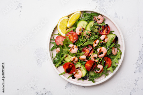 Arugula, cucumber, tomato and shrimp salad with soy sauce on a ceramic plate. Selective focus. Top view.