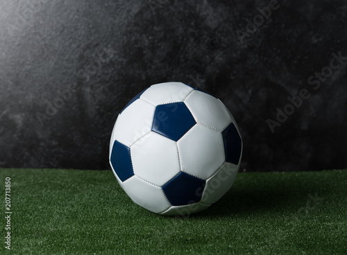 Soccer ball on green grass against black cement wall