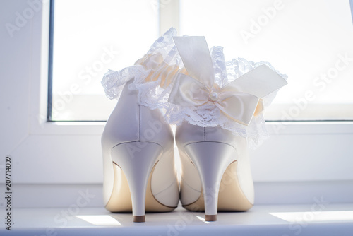 White wedding shoes of the bride and garter by the window photo