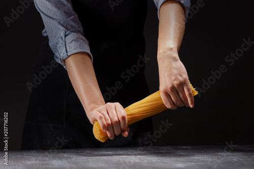 chef in an apron breaks a handful of raw Italian spaghetti