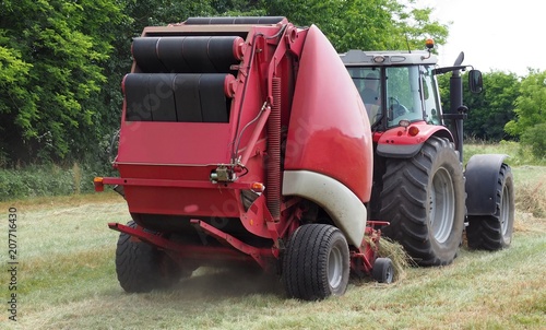 Hay baler machine pulled by a red tractor on a freshly cut field photo