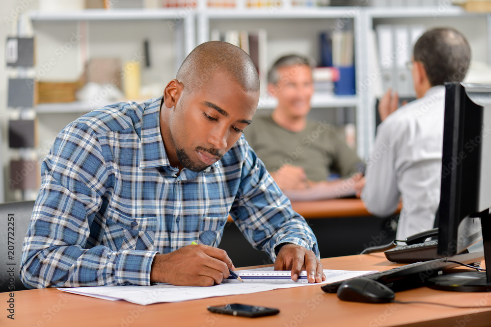 Man sat at desk working on blueprints Man sat at desk working on blueprints
