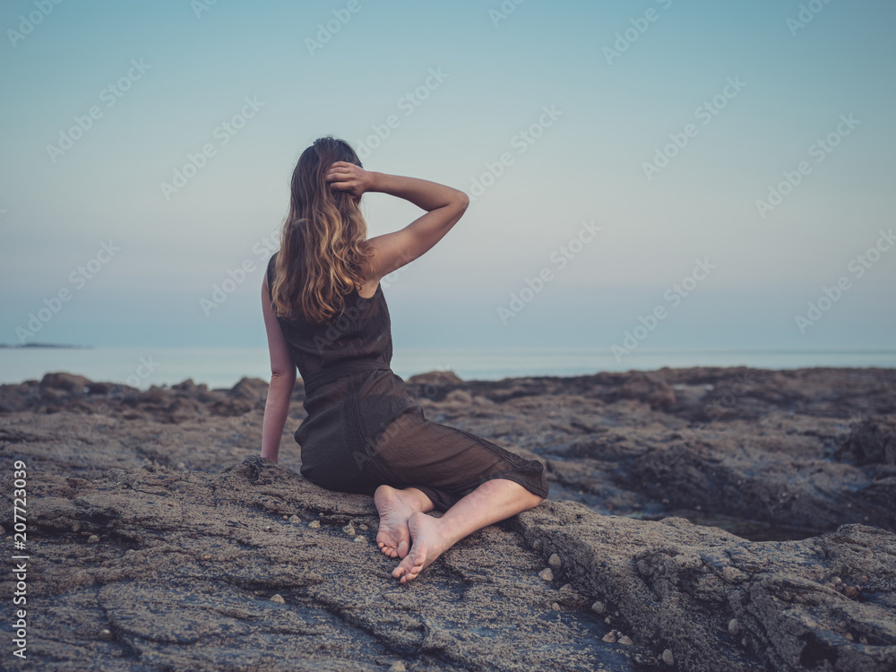 Young woman sitting on coast at sunset
