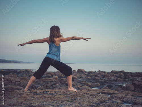 Woman in yoga warrior pose on coast at sunset