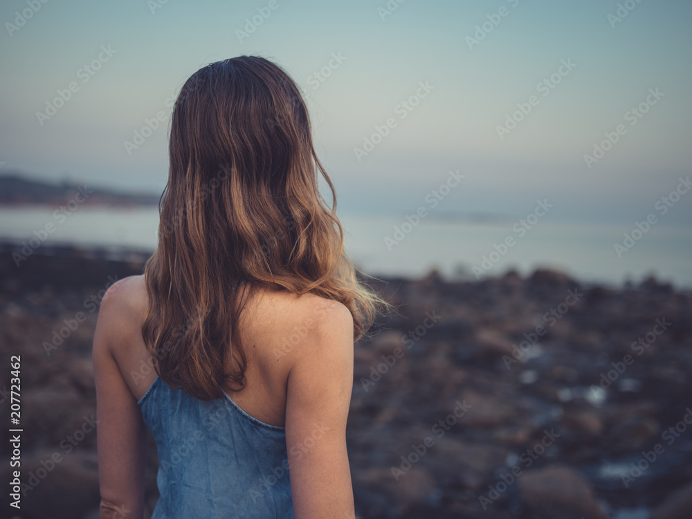Young woman standing on coast at sunset Young woman standing on coast at sunset