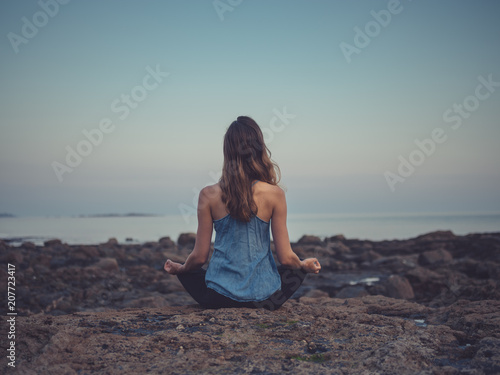 Young woman meditating on coast at sunset