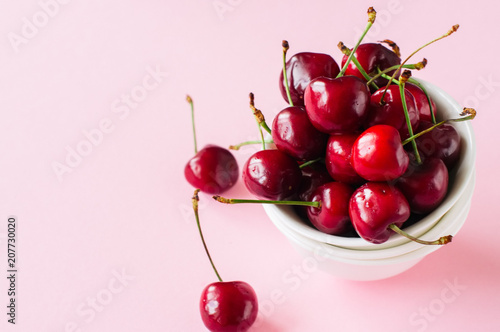 Heap of fresh ripe red cherries in a white bowl on a light pink background. Top view and copy space. Organic food concept.