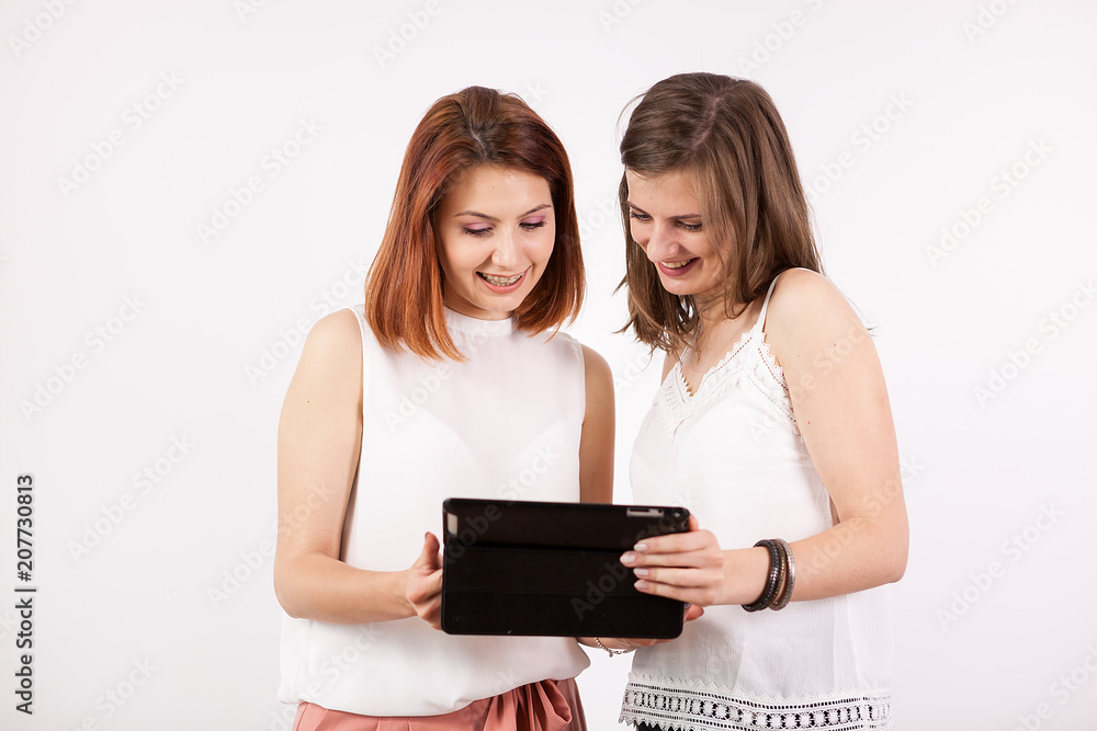 Portrait of two gorgeous women holding a tablet PC and looking at it while smiling Portrait of two gorgeous women holding a tablet PC and looking at it while smiling