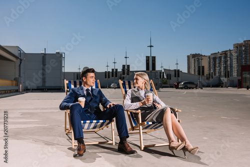 young business people relaxing on sunbeds with coffee to go on parking
