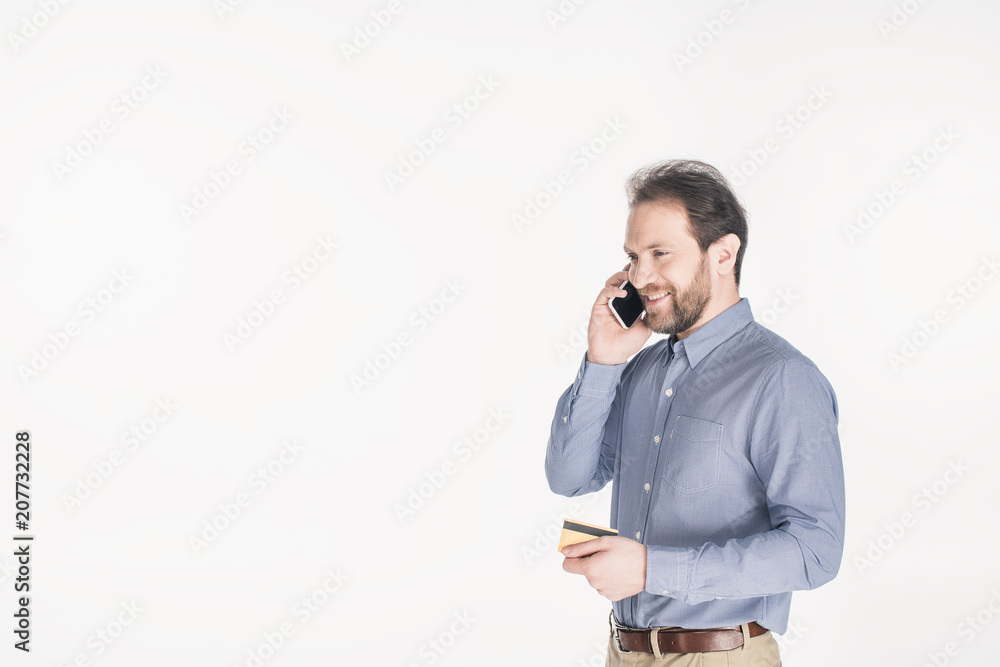 side view of bearded man with credit card in hand talking on smartphone isolated on white side view of bearded man with credit card in hand talking on smartphone isolated on white