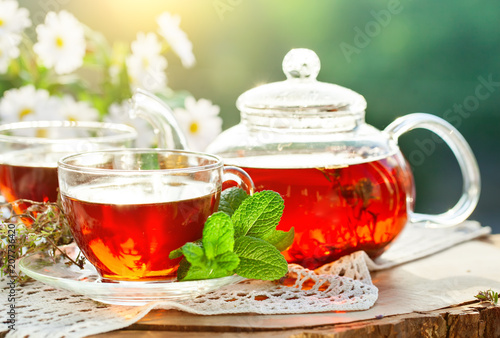 Cup with hot tea with mint and a thyme on a wooden table in a summer garden.