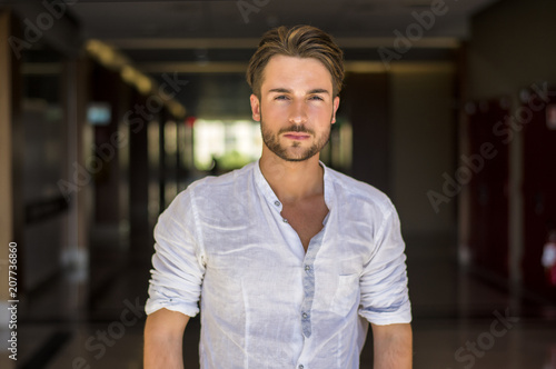Waist Up Portrait of Attractive Young Man Wearing Shirt Standing Looking Thoughtful in Hallway of School or Shopping Mall