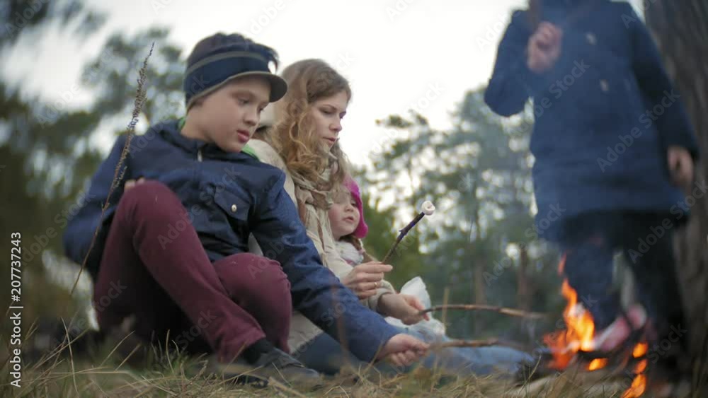 Happy family of tourists on a journey. Mom and children fry marshmallows on the fire near the tent Happy family of tourists on a journey. Mom and children fry marshmallows on the fire near the tent