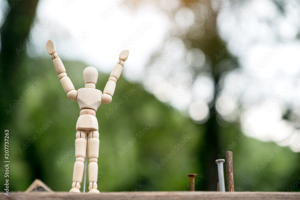 Obraz premium Closeup image of wooden figure model of a man rising hands and standing on wooden table with blur background