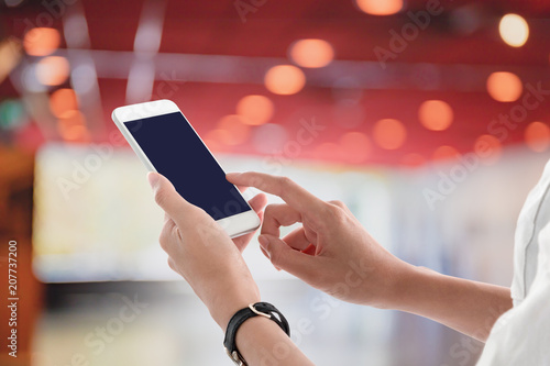 Woman hands holding and using smartphone with blank screen for your text or advertising isolated on blurred cinema theater interior background.Mock up phone mobile concept.