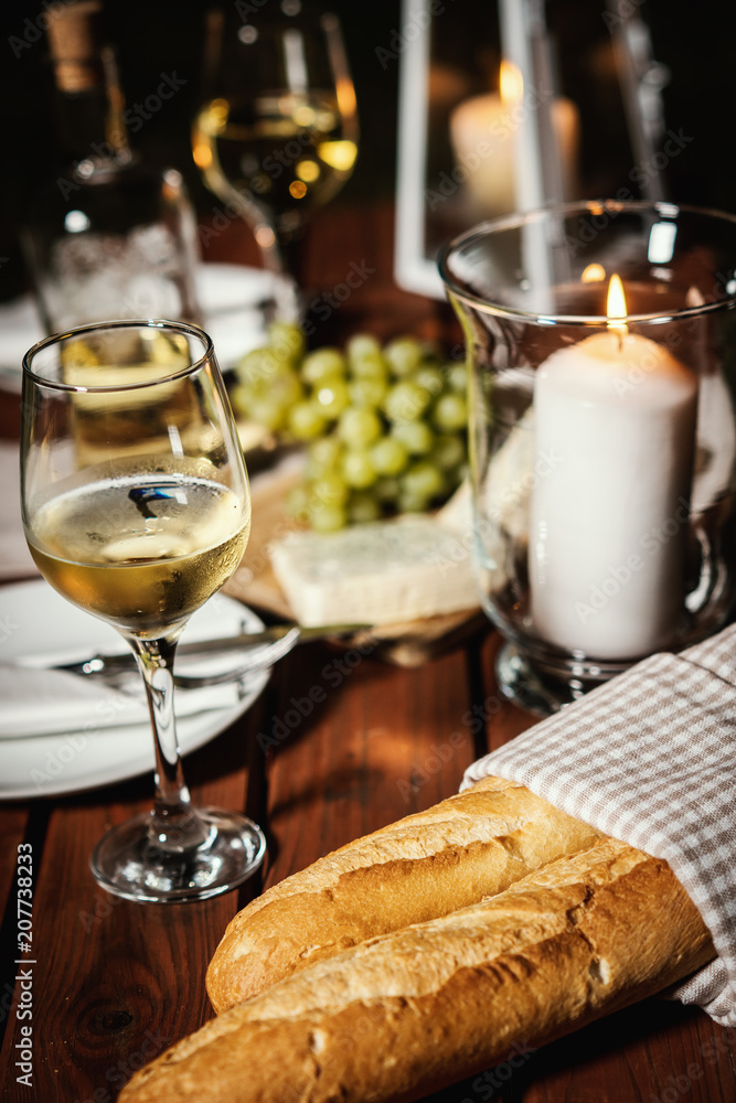 romantic dinner with a glass of wine, a baguette and snacks on an old wooden table on a summer evening