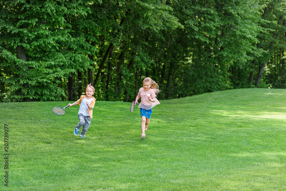 cute little kids with badminton rackets running together in park cute little kids with badminton rackets running together in park