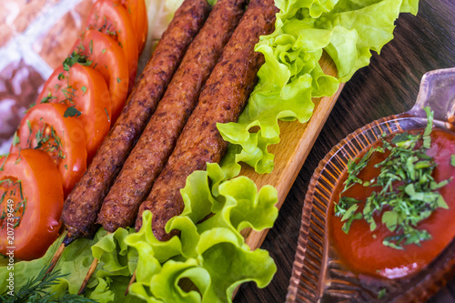 Lulya-kebab. Shish kebab on a stick, minced meat. Traditional Caucasian dish. On a cutting board, with green salad, ketchup, spices. photo