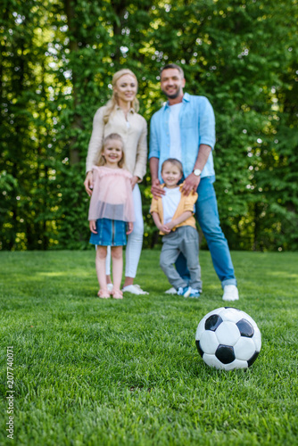 close-up view of soccer ball on grass and happy family standing together in park