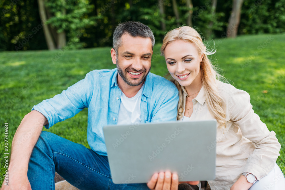 happy young couple using laptop while sitting together in park happy young couple using laptop while sitting together in park
