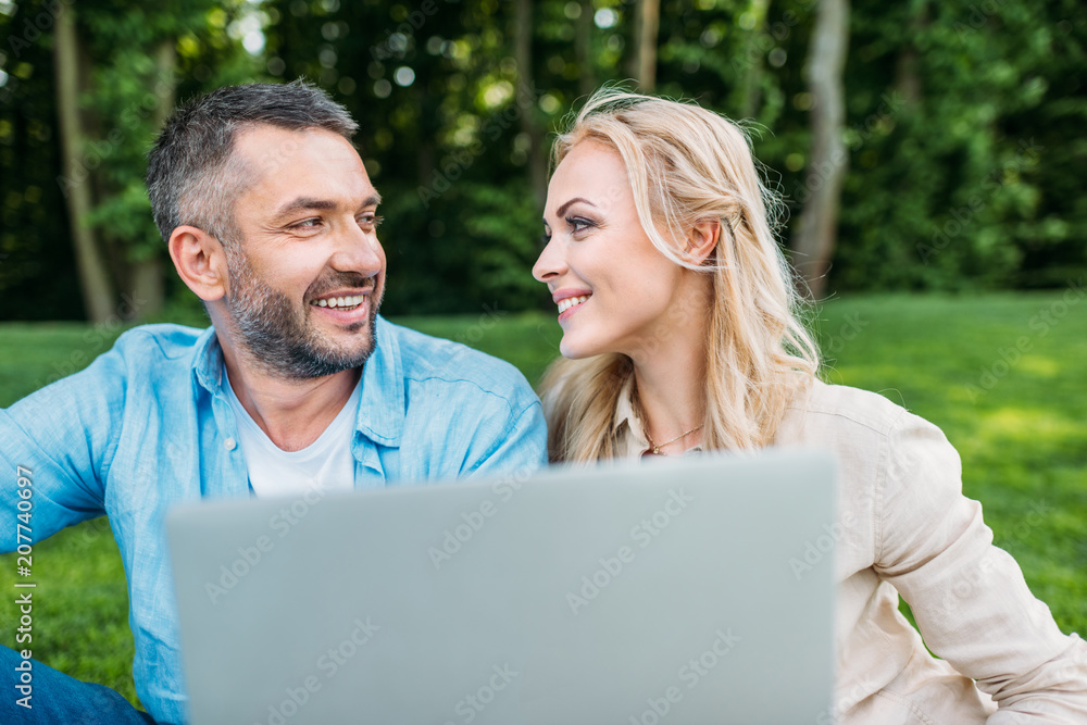 happy couple using laptop and smiling each other in park happy couple using laptop and smiling each other in park