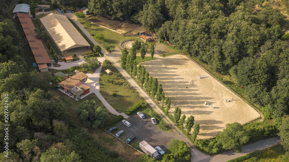 Aerial view of a riding field with fence and obstacles to train horses. In this sports facility, tournaments and horse racing courses are organized. The sports center is located in nature.