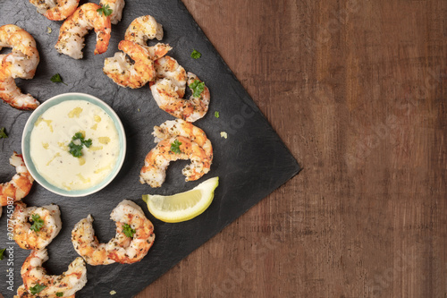 Overhead photo of plate of cooked shrimps on a dark rustic background, with a sauce, with copy space