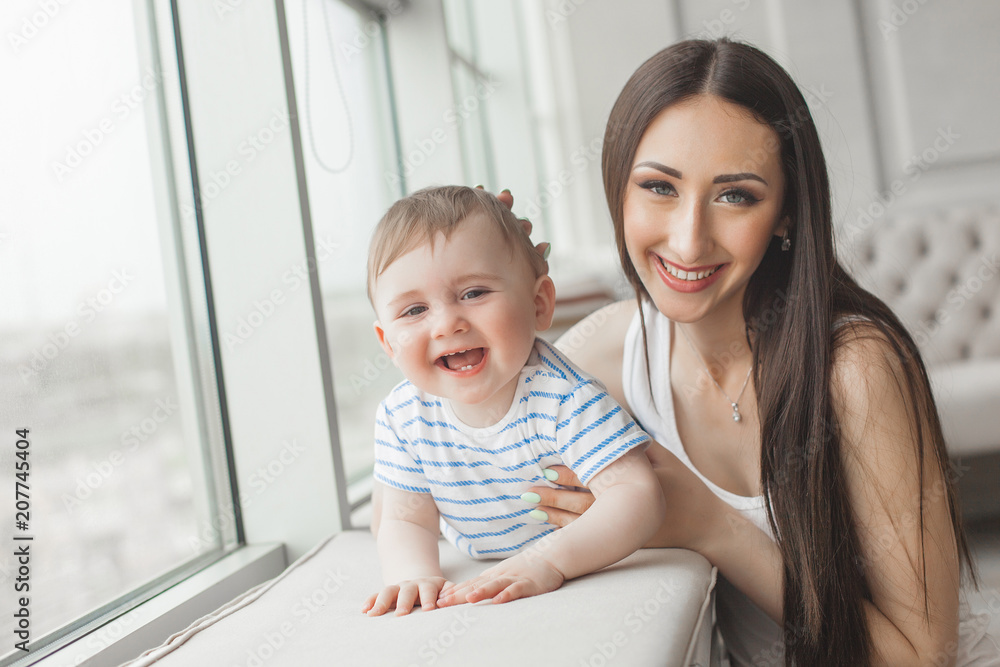 Fototapeta premium Young pretty mother playing with her little son. Cheerful family smiling at camera