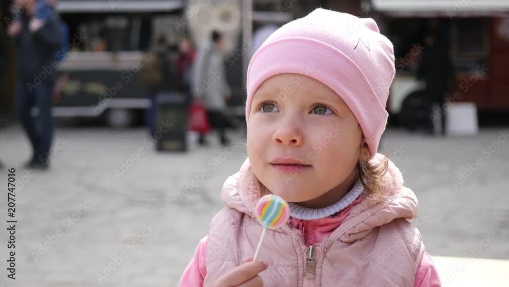 Child girl portrait lick a sweet candy lollipop on a stick at food fair slow motion Child girl portrait lick a sweet candy lollipop on a stick at food fair slow motion