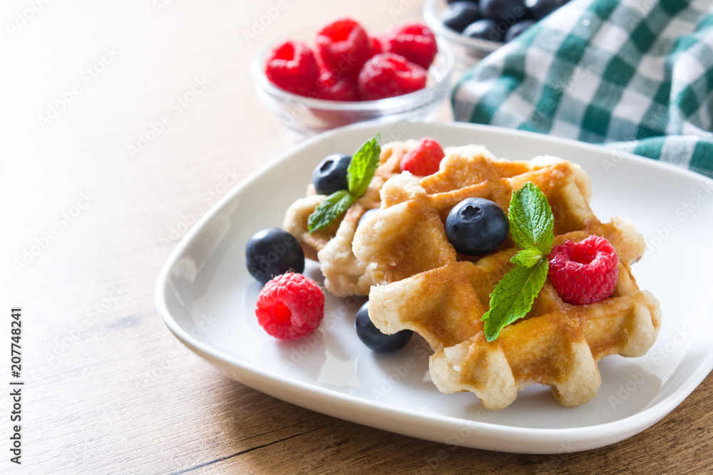 Traditional belgian waffles with blueberries and raspberries on wooden table
