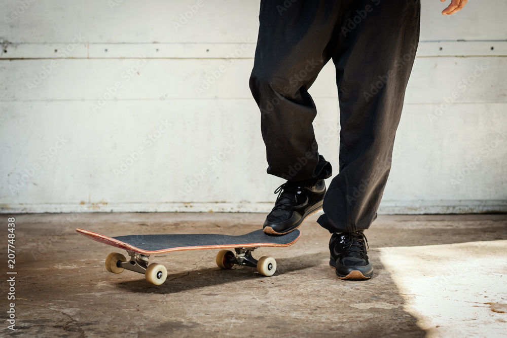 man in black pants stands with one foot on a skateboard in a concrete skatepark man in black pants stands with one foot on a skateboard in a concrete skatepark