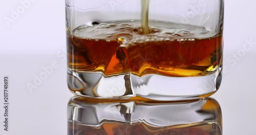 close up of whisky pouring in a glass on a white reflective surface
