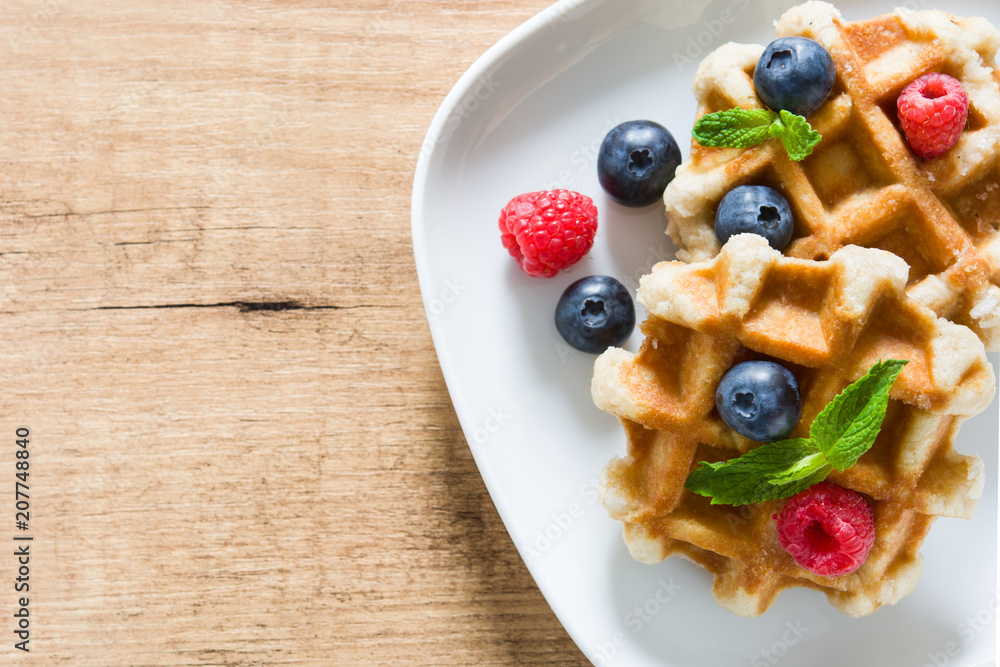 Traditional belgian waffles with blueberries and raspberries on wooden table. Top view. Copyspace Traditional belgian waffles with blueberries and raspberries on wooden table. Top view. Copyspace